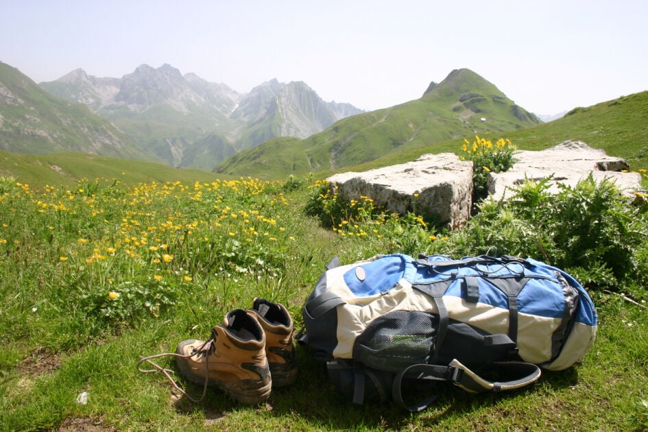 Utopian field with mountains and flowers showing hiking boots in the foreground with a hiking backpack.